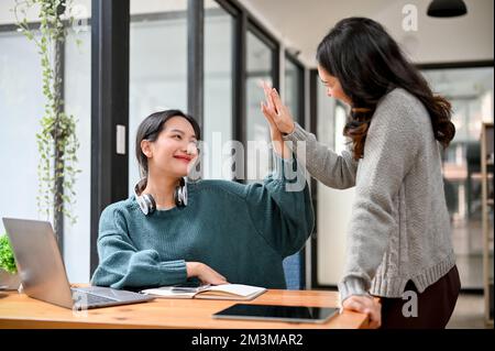 Une femme d'affaires asiatique heureuse et joyeuse qui donne cinq hauts à sa collègue au bureau. travail d'équipe, amitié, collaboration. Banque D'Images