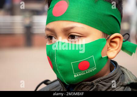 Narayanganj, Dhaka, Bangladesh. 16th décembre 2022. Un enfant porte un masque facial et un bandeau sur le thème du drapeau du Bangladesh pour célébrer le jour de la victoire de 52nd, qui marque la fin d'une guerre amère de neuf mois d'indépendance par rapport au Pakistan, à Narayanganj, au Bangladesh. Le Bangladesh célèbre le 52nd anniversaire de sa victoire nationale, en rappelant les vaillants combattants de la liberté qui ont combattu et fait le sacrifice ultime pour libérer le pays des forces pakistanaises. Les gens de tous les milieux se rassemblent au Narayanganj Central Shaheed Minar dans la matinée pour marquer le jour le plus précieux du peuple Bangali Cr Banque D'Images