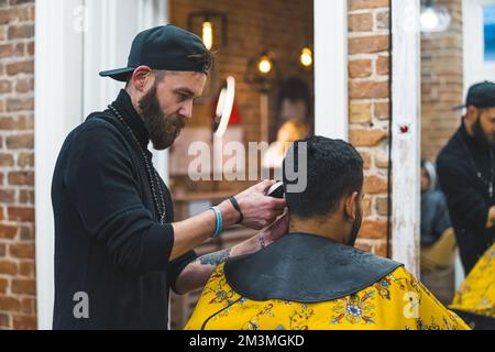 coiffeur professionnel avec chapeau noir qui grognera les cheveux de son client dans un salon de coiffure. Photo de haute qualité Banque D'Images