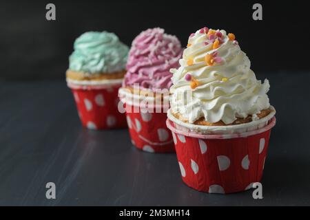 trois cupcakes blanc rose vert avec des arrosettes sur fond noir. Voeux anniversaire de vacances. Banque D'Images