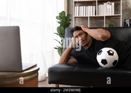 Un jeune fan de football asiatique a été déçu et irrité de regarder un match de football sur le canapé Banque D'Images