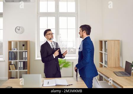 Deux jeunes gens d'affaires qui ont une conversation en se tenant près d'un bureau Banque D'Images