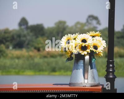 Arrosoir en forme de pot de fleurs et plantes jaunes placées près de la rivière. Banque D'Images