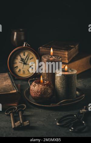 Bougies, livres anciens, vieille horloge et vieilles clés rouillées dans le style vintage sur fond noir Banque D'Images