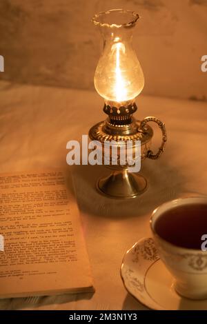 photo sur la table est une lampe à huile brûlante à côté d'une tasse de thé rétro et d'un vieux livre ouvert Banque D'Images