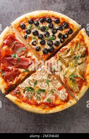 Pizza fraîche du four quatre saisons avec tomates, mozzarella, champignons, artichauts, jambon et olives en gros plan sur la table. Vue verticale du dessus avant Banque D'Images