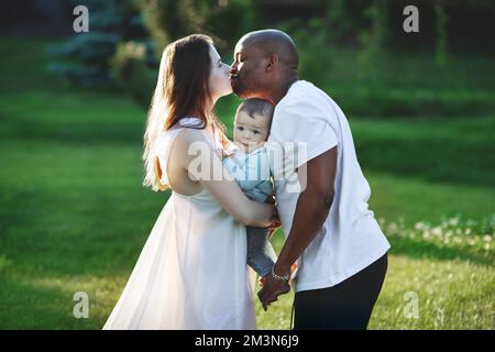 Famille multiethnique. La maman caucasienne et le papa afro-américain embrassent et tiennent dans les bras petit enfant. Parents, Portrait de maman, papa et bébé sur les mains Banque D'Images