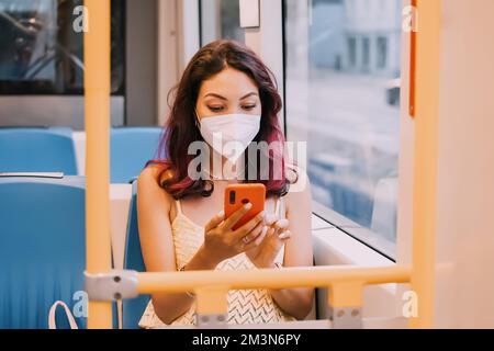 Une jeune fille portant un masque de protection lors d'une épidémie de maladie respiratoire infectieuse dans les transports publics utilise un téléphone portable Banque D'Images