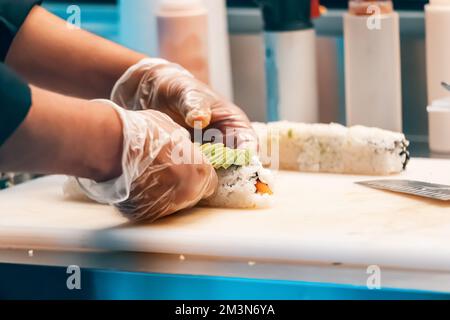 Le chef porte des gants pour cuisiner des petits pains à sushis au restaurant Banque D'Images