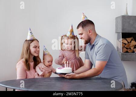 Bonne famille célébrant l'anniversaire de l'enfant. Mère, père et deux petites filles avec gâteau et bougies isolées sur fond blanc Banque D'Images