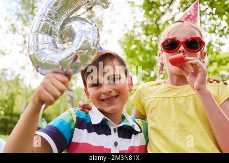 Une fille soufflait de soufflage par un ami masculin avec le numéro six dans la fête d'anniversaire au parc Banque D'Images