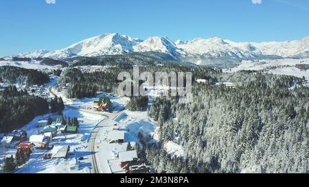 Une vue aérienne de la zone rurale avec des forêts enneigées et des bâtiments en hiver au Monténégro Banque D'Images
