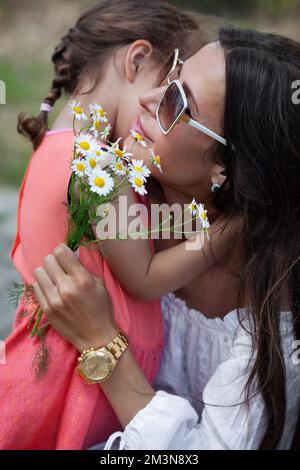 Gros plan portrait de la mère épouse la fille enfant et tient des fleurs de camomille. Fête des mères Banque D'Images