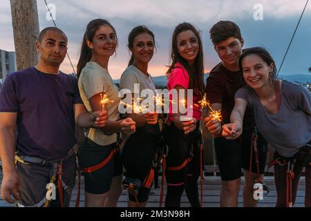 Jeune groupe de grimpeurs de rock qualifiés ayant du plaisir et jouant avec des sparkles avec le coucher du soleil en arrière-plan Banque D'Images