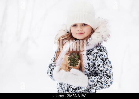 Jolie petite fille avec cadeau de noël dans des vêtements chauds en hiver sur fond de neige blanc. Extérieur portrait d'hiver beau petit modèle enfant avec p Banque D'Images