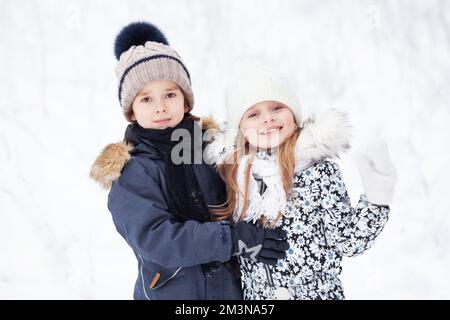 Portrait de beaux enfants gaies sur fond de neige blanche. Jolis modèles portant des vestes et des chapeaux d'hiver Banque D'Images