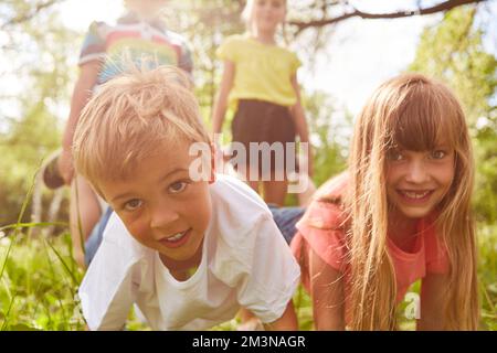 Portrait d'enfants heureux en compétition pendant la course de brouettes dans le parc le jour ensoleillé Banque D'Images