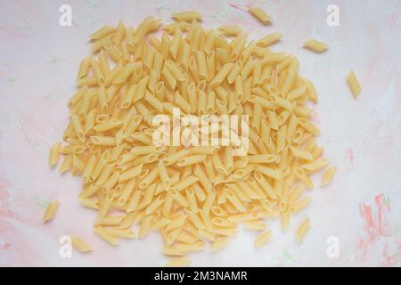 Pile de pâtes italiennes traditionnelles brutes de penne sur fond de piink. Ingrédient pour la cuisson. Gros plan, vue de dessus Banque D'Images