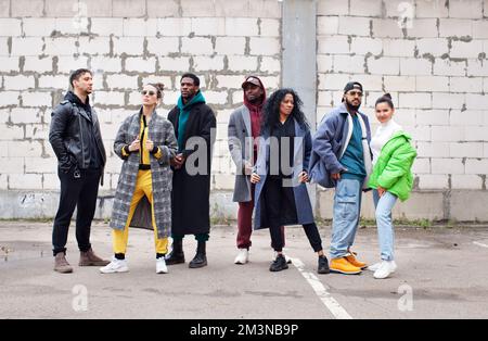 Groupe multiethnique de jeunes hippies se dresse sur la rue contre le mur de briques grises. Divers gens stylés dans les vêtements d'extérieur, la culture de jeunesse Banque D'Images