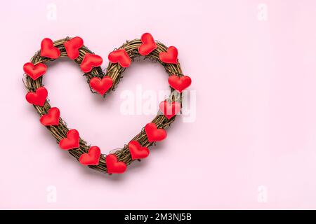 Couronne en rotin en forme de coeur décorée de coeurs rouges sur fond rose vue du dessus plat Lay carte de vacances texte bonne Saint-Valentin, amour concept copie s. Banque D'Images