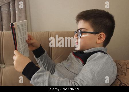 Livre de lecture, petit enfant en lunettes lecture livre à la maison dans sa chambre. Banque D'Images