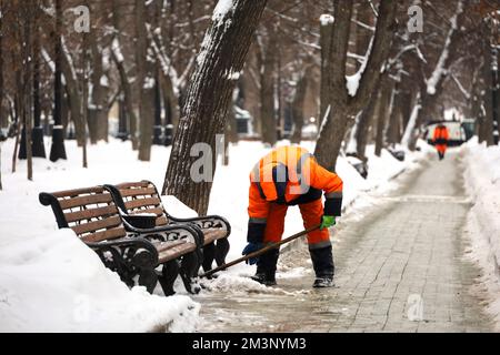 Un employé nettoie la neige dans les rues de la ville après une chute de neige. Homme avec une pelle dans le parc d'hiver Banque D'Images