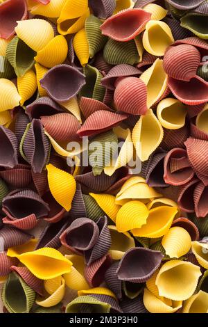 Fond de pâtes coloré. Vue de dessus des coquilles de pâtes cinq couleurs sur fond de pierre blanche. Pâtes au curcuma, aux épinards, à la betterave et à la carotte noire. Banque D'Images