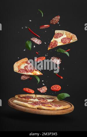 pizza volante avec ingrédients sur fond noir Banque D'Images