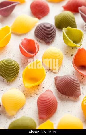 Vue de dessus des coquilles de pâtes cinq couleurs sur fond de pierre blanche. Pâtes au curcuma, aux épinards, à la betterave et à la carotte noire. Prise de vue macro Banque D'Images