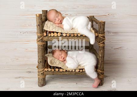 Petits garçons jumeaux nouveau-nés en bodys blancs sur fond de bois clair. Banque D'Images