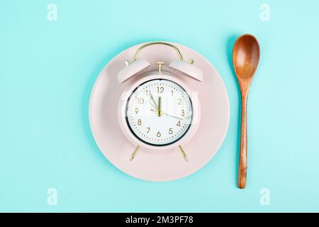 Réveil sur une assiette avec une cuillère dans le style rétro ancien, couleur pastel, heure de se réveiller le matin, déjeuner, prendre une pause Banque D'Images