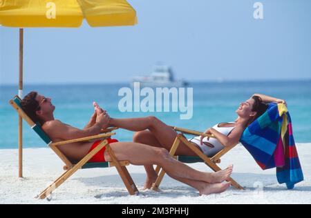 Couple allongé sur des chaises longues à la plage pendant que l'homme fait un massage du pied de femme Banque D'Images