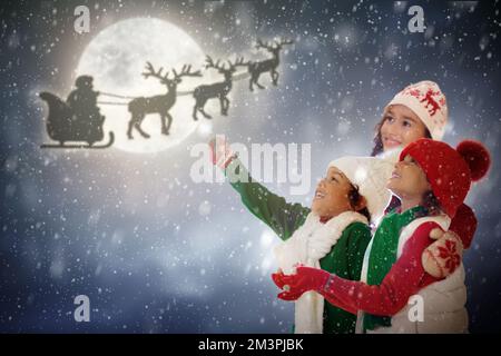 Les enfants regardent le Père Noël voler dans le ciel la veille de Noël. Les enfants regardent le renne et le Père Noël livrer des cadeaux le soir de Noël. Hiver neige amusant. Banque D'Images