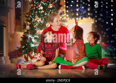 Famille sous un arbre de Noël. Mère et enfants avec cadeaux dans la salle de séjour décorée avec cheminée. Fête de Noël avec à la maison. Enfant avec cadeaux Banque D'Images