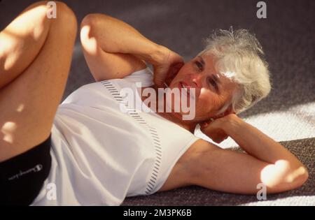 Une femme plus âgée se pose sur le dos pour faire des exercices Banque D'Images