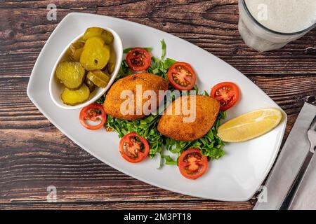 Kibbeh ou icli kofte sur une assiette en porcelaine blanche avec cornichons et salade Banque D'Images