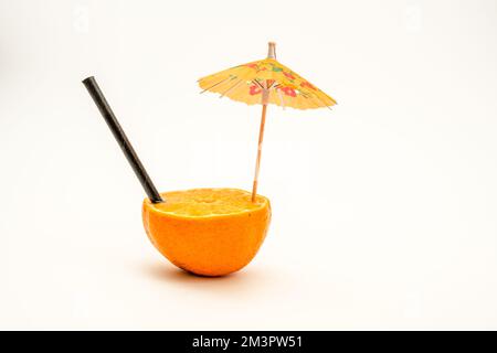 parasol orange coloré et paille de bambou noire dans la moitié d'une orange Banque D'Images