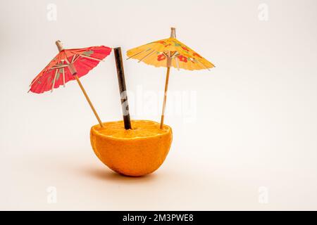 deux boissons de fête orange et rouge colorées, le parasol et la paille de bambou noire dans la moitié d'une orange Banque D'Images