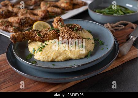 Pilons de poulet marinés avec de la pâte d'harissa. Garnie de graines de sésame et servie avec de la polenta et des haricots verts sur une assiette Banque D'Images