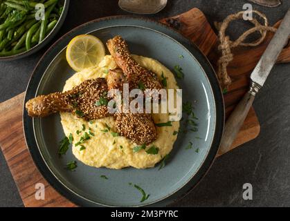 Pilons de poulet marinés avec des épices de harissa et cuits avec des graines de sésame. Servi avec de la polenta crémeuse et des haricots verts sur une assiette Banque D'Images