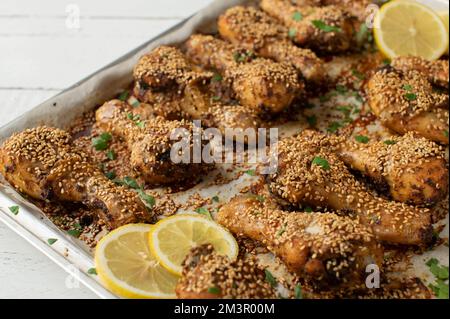 Pilons de poulet épicés avec pâte de harissa et graines de sésame sur une plaque de cuisson Gros plan, vue de face avec arrière-plan flou Banque D'Images