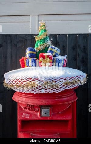 Surmatelas de boîte postale de Noël, crochet ou tricoté arbre de noël et présente sur boîte aux lettres rouge royal, Angleterre, Royaume-Uni, en décembre 2022 Banque D'Images