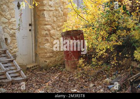 Un baril rouge rouillé dans une cour avec des glands sur le sol. Banque D'Images