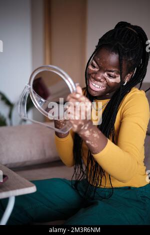 Femelle ethnique positive avec le vitiligo appliquant le maquillage à la maison Banque D'Images