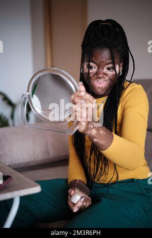 Femme noire avec vitiligo faisant le maquillage dans le salon Banque D'Images