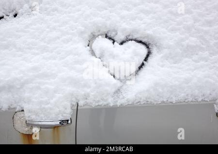 Signe d'amour en forme de coeur, dessiné sur une voiture enneigée. Forme de coeur dessinée à la main dans la neige fraîche. Symbole de l'amour en hiver Banque D'Images