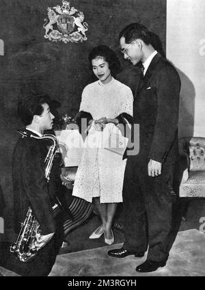 Une visite officielle de l'Australie par le roi Bhumibol Adulyadej (Rama IX) (1927-) et la reine Sirikit (1932-) de Thaïlande. Le couple royal reçoit l'hommage d'un étudiant thaïlandais, M. D. Juejok, à Sydney, en Nouvelle-Galles du Sud. Le Roi, un musicien prend le temps d'avoir une conversation avec le saxophoniste à genoux, qui venait de jouer l'hymne national thaïlandais. Date: 1962 Banque D'Images