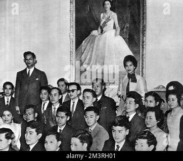 Une visite officielle de 8 jours en Nouvelle-Zélande par le roi Bhumibol Adulyadej (Rama IX) (1927-) et la reine Sirikit (1932-) de Thaïlande - photo prise à la Maison du gouvernement, Wellington, alors qu'un grand groupe d'étudiants thaïlandais se réunissent autour du roi et de la reine, sous un portrait complet de la reine Elizabeth II Date: 1962 Banque D'Images
