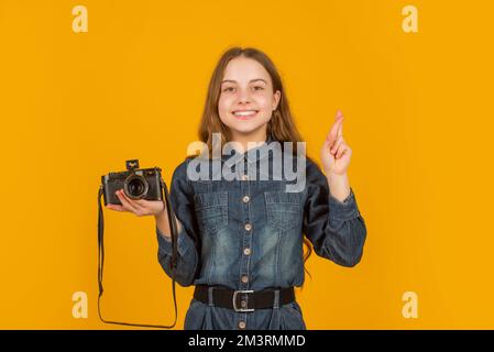 Bonne fille photographe superstitititieuse tenant photo appareil en gardant les doigts croisés, chance Banque D'Images