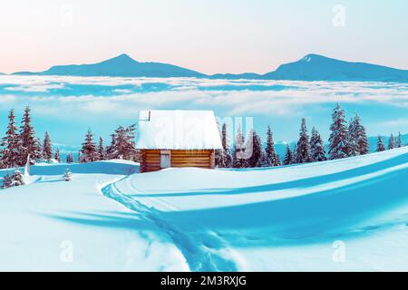 Paysage d'hiver fantastique avec maison en bois et pics de montagne dans la brume dans les montagnes enneigées. Concept de vacances de Noël. Montagne des Carpates, Ukraine, Europe Banque D'Images